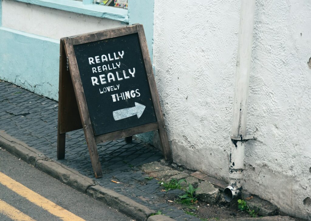 Wooden A-board sign with hand-written lettering on a cobbled pavement outside a shop