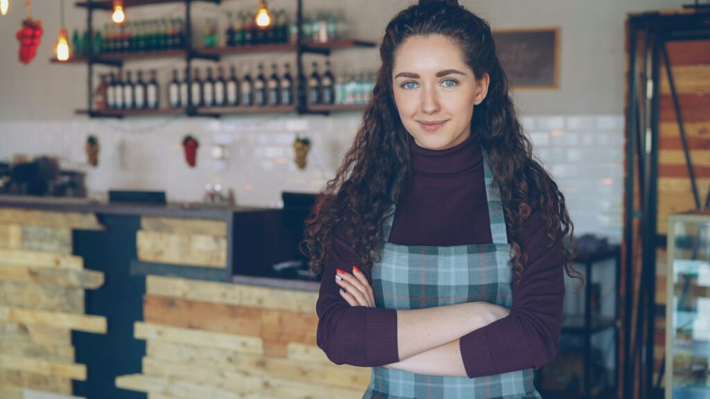 Smiling woman standing in her coffee shop, representing the small business owners government spending aims to support