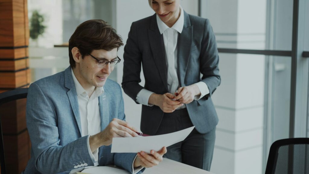 Two business colleagues reviewing documents together at a table, discussing reports and costs