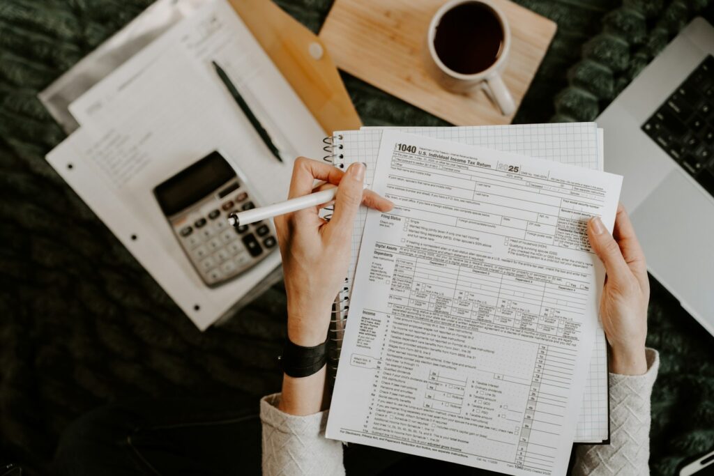 Person reviewing documents with a calculator and laptop while preparing year end accounts