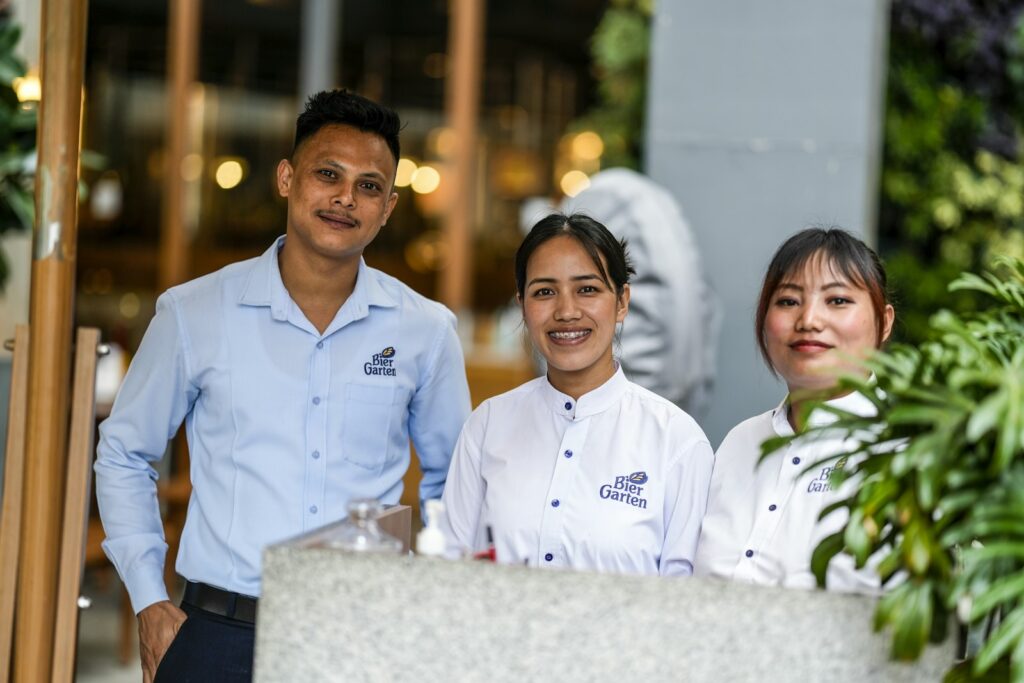 Three smiling restaurant staff members standing together behind a counter, showing a team working well