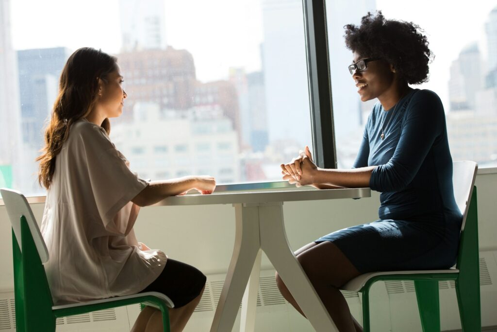 Two women sitting beside a table and talking, like a business coaching conversation