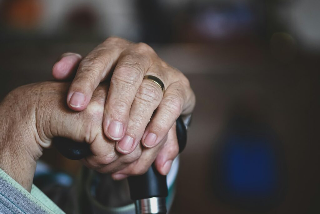 Wrinkled hands with a gold ring on a black cane handle, evoking care for older people